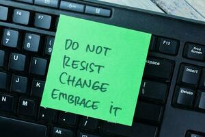 Concept of Do Not Resist Change Embrace it write on sticky notes isolated on Wooden Table. photo