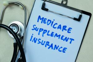 Concept of Medicare Supplement Insurance write on book with stethoscope isolated on Wooden Table. photo