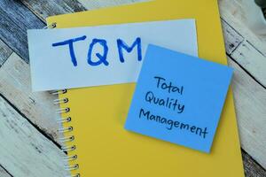 Concept of TQM - Total Quality Management write on sticky notes isolated on Wooden Table. photo