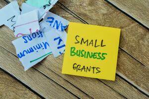 Concept of Small Business Grants write on sticky notes isolated on Wooden Table. photo