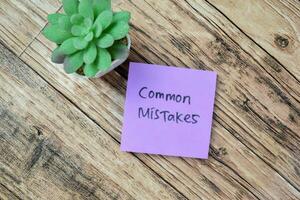 Concept of Common Mistakes write on sticky notes isolated on Wooden Table. photo