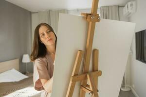 Young woman artist painting on canvas on the easel at home in bedroom - art and creativity concept photo