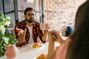 Happy indian couple having breakfast and small talk together in the kitchen - friendship, dating and family photo