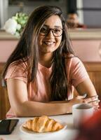 retrato inteligente confidente sonriente milenario indio mujer. atractivo joven hindú adolescente estudiante niña persona de libre dedicación durante desayuno té y cuerno foto