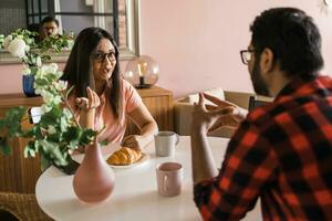 Happy couple eating breakfast and talking at dining table in morning. Indian girl and latino guy. Relationship and diversity concept photo