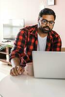 technology remote job and lifestyle concept - happy indian man in glasses with laptop computer working at home office photo