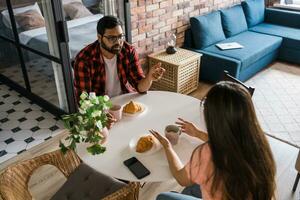 Happy couple eating breakfast and talking at dining table in morning. Indian girl and latino guy. Relationship and diversity concept photo
