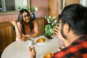Happy indian couple having breakfast and small talk together in the kitchen - friendship, dating and family photo