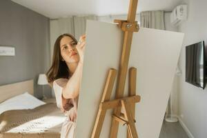 joven mujer artista pintura en lona en el caballete a hogar en dormitorio - Arte y creatividad concepto foto