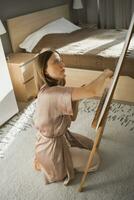 Young woman artist painting on canvas on the easel at home in bedroom - art and creativity concept photo