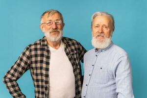 Portrait two elderly man friends standing over blue background - friendship, aged and senior people photo