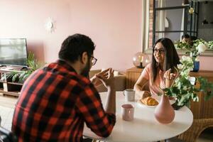 Happy couple eating breakfast and talking at dining table in morning. Indian girl and latino guy. Relationship and diversity concept photo