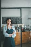 Portrait of happy waitress standing at restaurant entrance with open sign, Portrait of young business woman attend new customers in her coffee shop. photo