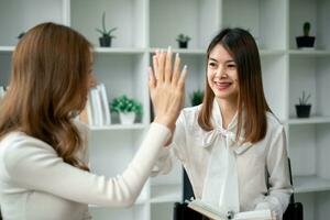 Businesswoman giving a high five to female colleague in meeting. Business professionals high five during a meeting in boardroom. photo