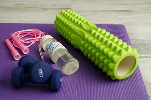 massage roller, dumbbells, water bottle and jump rope on a gym mat photo
