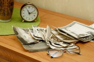 a stack of old black and white photographs scattered on a table with glasses and an alarm clock, memories, the past photo