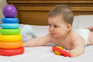 baby girl in a diaper on the bed reaches for toys photo