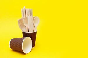 disposable wooden spoons, forks and knives in a paper cup on a yellow background with copyspace, recycled. photo