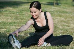 Young woman in black sportswear exercising outdoors. Fitness and healthy lifestyle concept. The white girl does sports in the park. photo