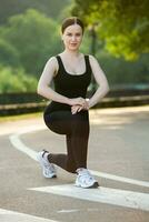 Young woman in black sportswear exercising outdoors. Fitness and healthy lifestyle concept. The white girl does sports in the park. photo