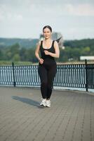 Young woman in black sportswear exercising outdoors. Fitness and healthy lifestyle concept. The white girl does sports in the park. photo