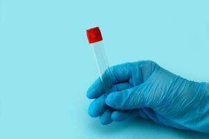 a gloved hand holds an empty test tube on a blue background with copy space, modern diagnostics photo