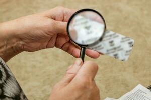 an elderly woman carefully examines a package of medicines through a magnifying glass photo