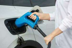 Young business woman refueling her electric car at a EV charging station. Concept of environmentally friendly vehicle. Electric car concept. Green travelling. photo