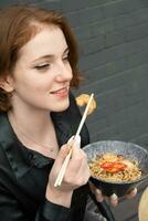 Beautiful young woman tastes udon noodles with shrimp and fried vegetables photo