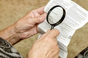 an elderly woman studies the instructions for the use of pills with a magnifying glass photo