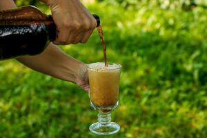 female hands pour cold kvass from a plastic bottle into a glass photo