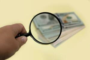 hand holding a magnifying glass over a blurred stack of banknotes photo