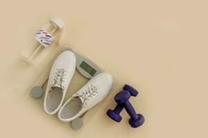 sneakers on floor scales, dumbbells and a bottle of water on a beige background with copy space photo