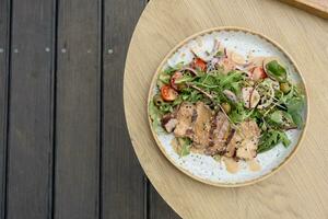 A plate with veal meat on greens with vegetables and olives under nut sauce on a wooden table top view photo