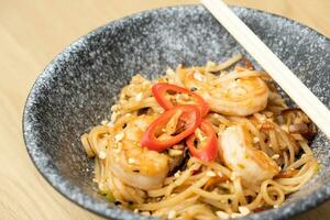 Udon noodles with shrimp and fried vegetables in a bowl top view photo
