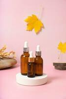 Glass dropper bottles with cosmetics oil or serum at autumn scene composition with podium photo