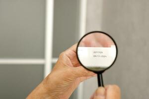 hands of an elderly man examining the expiration date of medicines with a magnifying glass photo