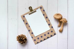 Empty paper with mushrooms  and cone on wooden background top view photo