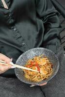 Udon noodles with shrimp and fried vegetables in a bowl in female hands with chopsticks photo
