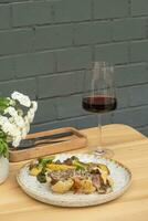 Baked meat in dough with potatoes and broccoli on wooden table with wineglass. photo