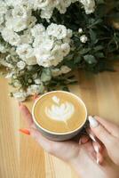 Coffee latte with female hand and flowers on cafe table photo