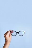 Eyeglasses in female hand on blue background.  Optical store, vision test, stylish glasses concept photo