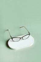 Podium with eyeglasses on pastel green background. Optical store, vision test, stylish glasses concept. photo