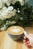 Coffee latte with female hand and flowers on cafe table photo