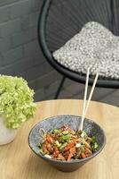 A bowl of udon noodles, veal and fried vegetables angle view on wooden table photo