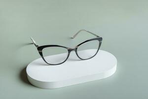 Podium with eyeglasses on pastel green background. Optical store, vision test, stylish glasses concept. photo