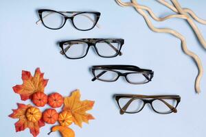 Glasses for vision on a blue background with autumn leaves and pumpkin. Optical store, vision test, stylish glasses concept photo