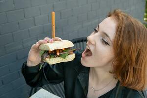 un joven mujer come un hamburguesa con carne en un verano terraza foto