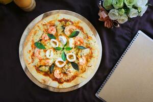 Delicious pizza with seafood on wooden stand, top view photo
