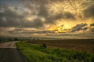 The landscape at the road through in the field with colorful clouds photo